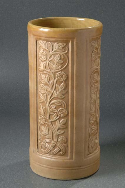 Tan ceramic cylinder with panels of relief carvings of vines.