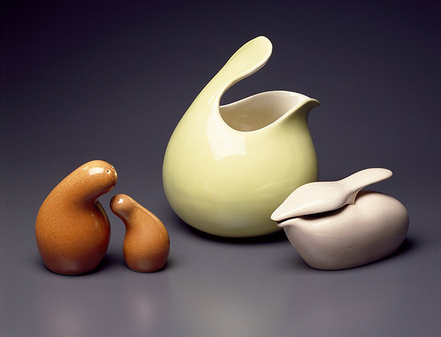 Orange salt-and-pepper shakers, a yellow pitcher, and a taupe oil pourer in fluid, round shapes sit against an indigo background.