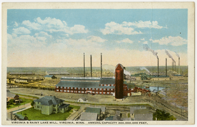 Color postcard showing the sprawling campus of a lumber mill, with a red two-story structure and silo in the middle ground and the horizon and sky in the background.
