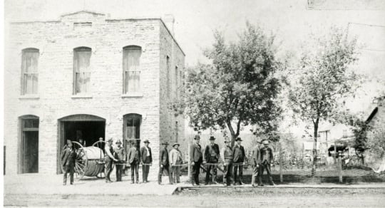 Black and white photograph of Cannon Falls firefighters posing in front of their headquarters.