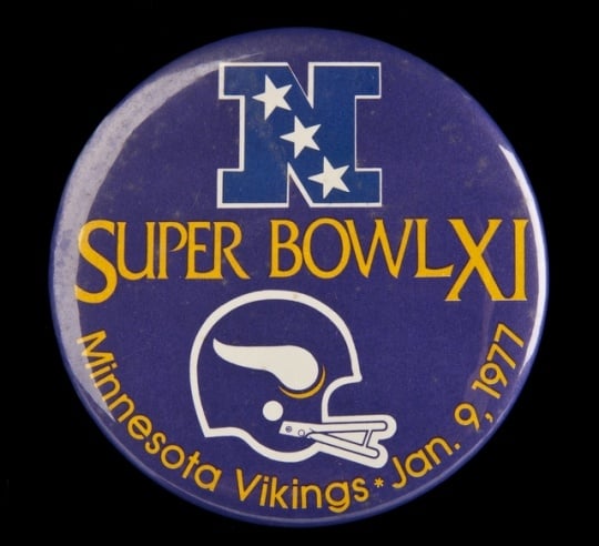 Color image of a plastic pin-back button commemorating the participation of the Minnesota Vikings in Super Bowl XI, played against the Oakland Raiders in Pasadena, California, 1977. The Raiders defeated the Vikings 32–14.