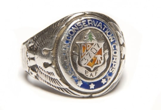 Color image of a Sterling silver Civilian Conservation Corps ring with CCC logo flanked by an eagle and shield on opposing ends. Logo is engraved with 3707/ and EAF. Worn by Fred Fretheim of Company 3707, Two Harbors, MN, ca. 1936–1937.