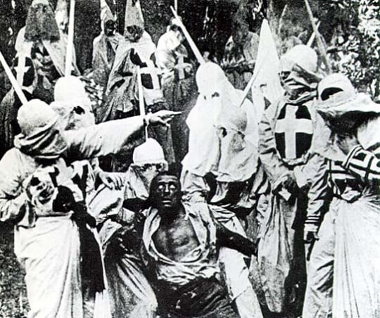 A scene from the movie Birth of a Nation (1915) featuring hooded Ku Klux Klan members surrounding Gus, a Black man portrayed in blackface by actor Walter Long.