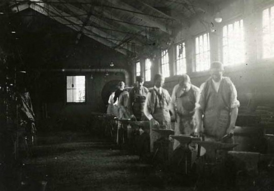 Black and white photograph of an Agriculture Extension, Short Course in Blacksmithing men at the forges, 1908.