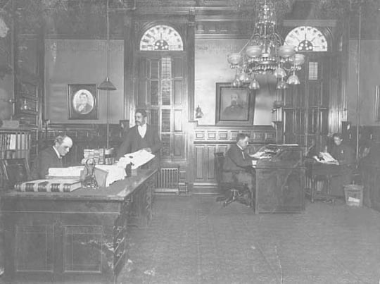 Minnesota governor's suite during John Lind's administration, c.1900. Pictured: John Lind at his desk G. P. Wade, postmaster of the Legislature L. A. Rosing, private secretary to the governor and an unidentified woman.