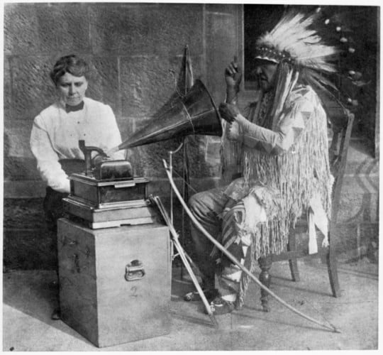 Black and white photograph of Frances Densmore with Mountain Chief who is interpreting a recording.