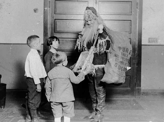 Black and white photograph of a worker dressed as Santa, passing out gifts at the Neighborhood House, c.1925.