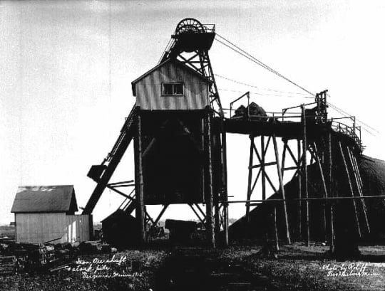 Black and white photograph of an iron ore shaft and stock pile in Virginia, Minnesota, 1915.