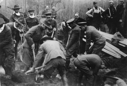 Black and white photograph of the Minnesota Home Guard digging graves after the fires, 1918. Minnesota Governor J.A.A. Burnquist looks on (hatless, at center back).
