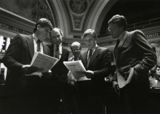 Black and white photograph of Ron Dicklich, William Luther, Allan Spear, Roger Moe, and Duane Benson reading a bill on the floor of the Minnesota Senate, 1988.