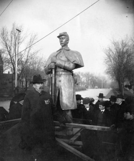 Black and white photograph of Josias King standing in front of a bronze statue patterned after his likeness, 1903.