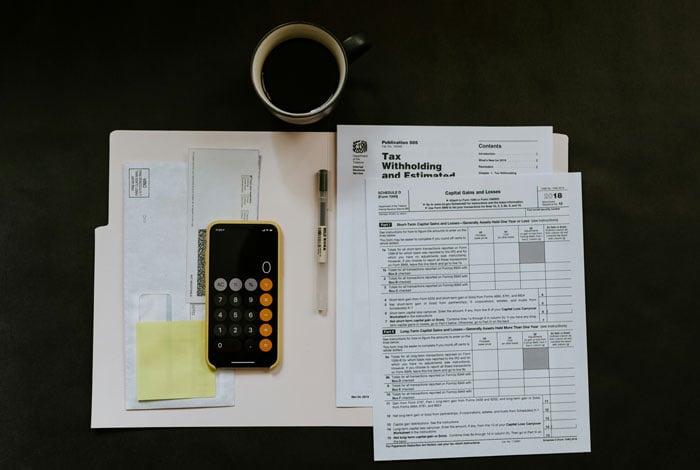 Black android smartphone near ballpoint pen tax withholding certificate on top of white folder.