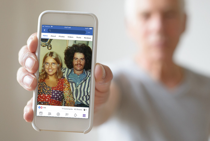 Man holding phone displaying old photo of himself with a woman.