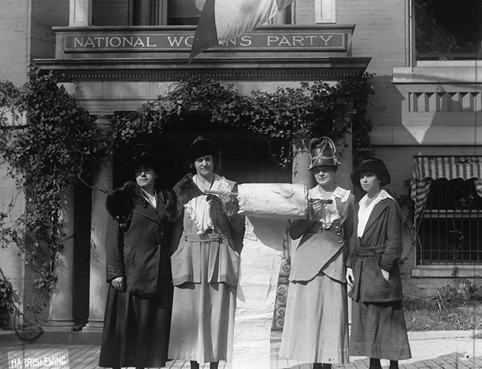 Four women standing with two holding a petition together.