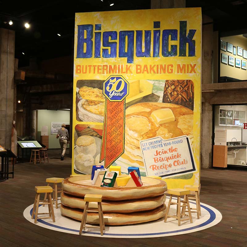 A large-scale model of a Bisquick box with a stack of model pancakes.