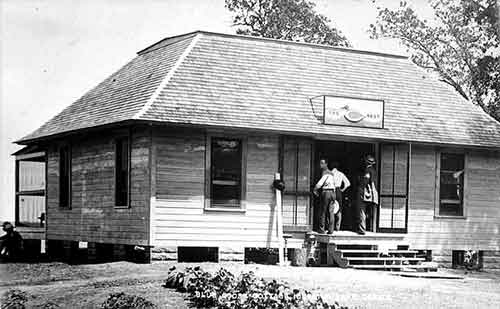 Blue Goose Cottage exterior near a lake with two people on the front stoop and a screened rear porch.