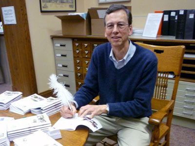 An author is signing books with a feathered pen.