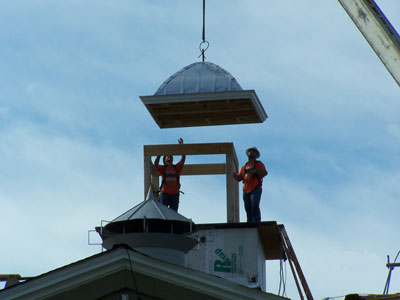 Cupola roof being move into place with two people signaling.