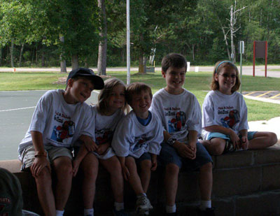 Five kids wearing the same kinds of t-shirts sitting in a park.