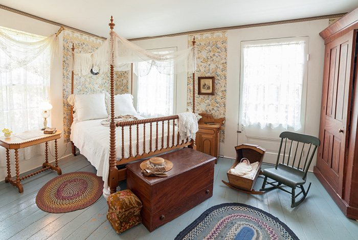 A bedroom with a bed, a cradle, a rocking chair and some other furniture.