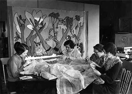 Four women sit at a table working with sewing lightweight fabric.