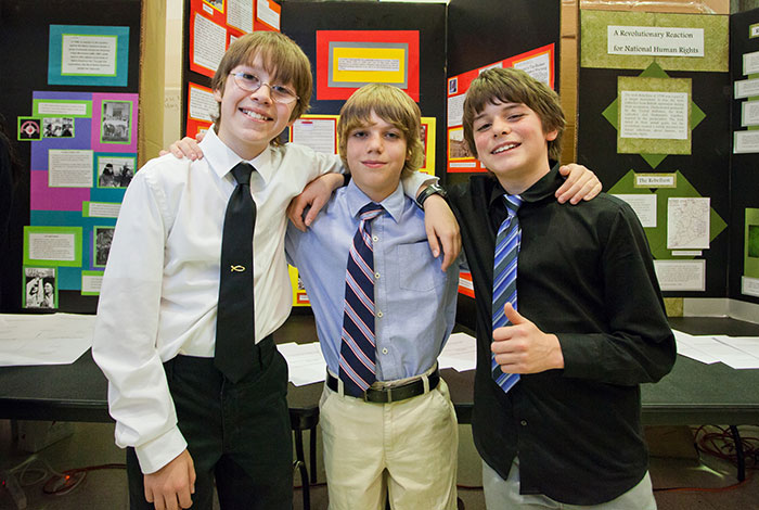 Three boys standing in front of poster board.