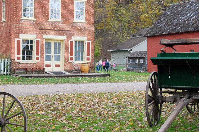A pair of wagons frame a group of visitors standing next to a brick building.