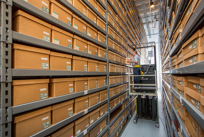 A photograph of a storage room with tall shelves of archival boxes