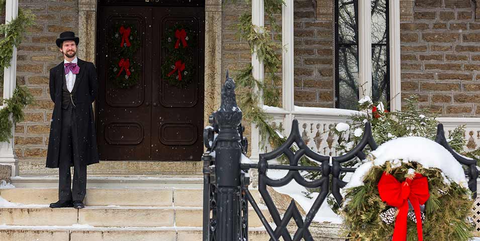 A man waiting on the steps in front of the door, with garland and wreath decorations