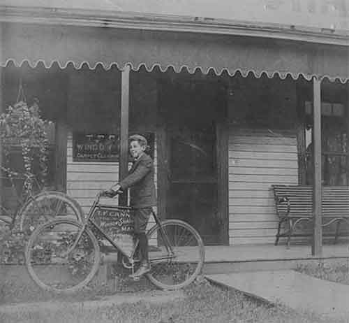 Boy standing with a bike in front of a building with scalloped awning.