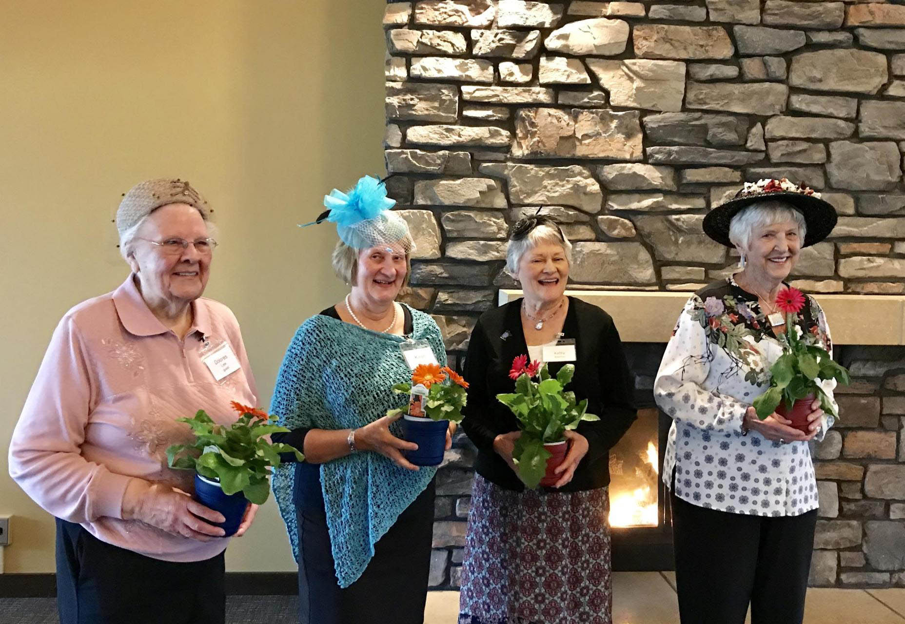 Four women wearing fancy hats and holding potted flowers.