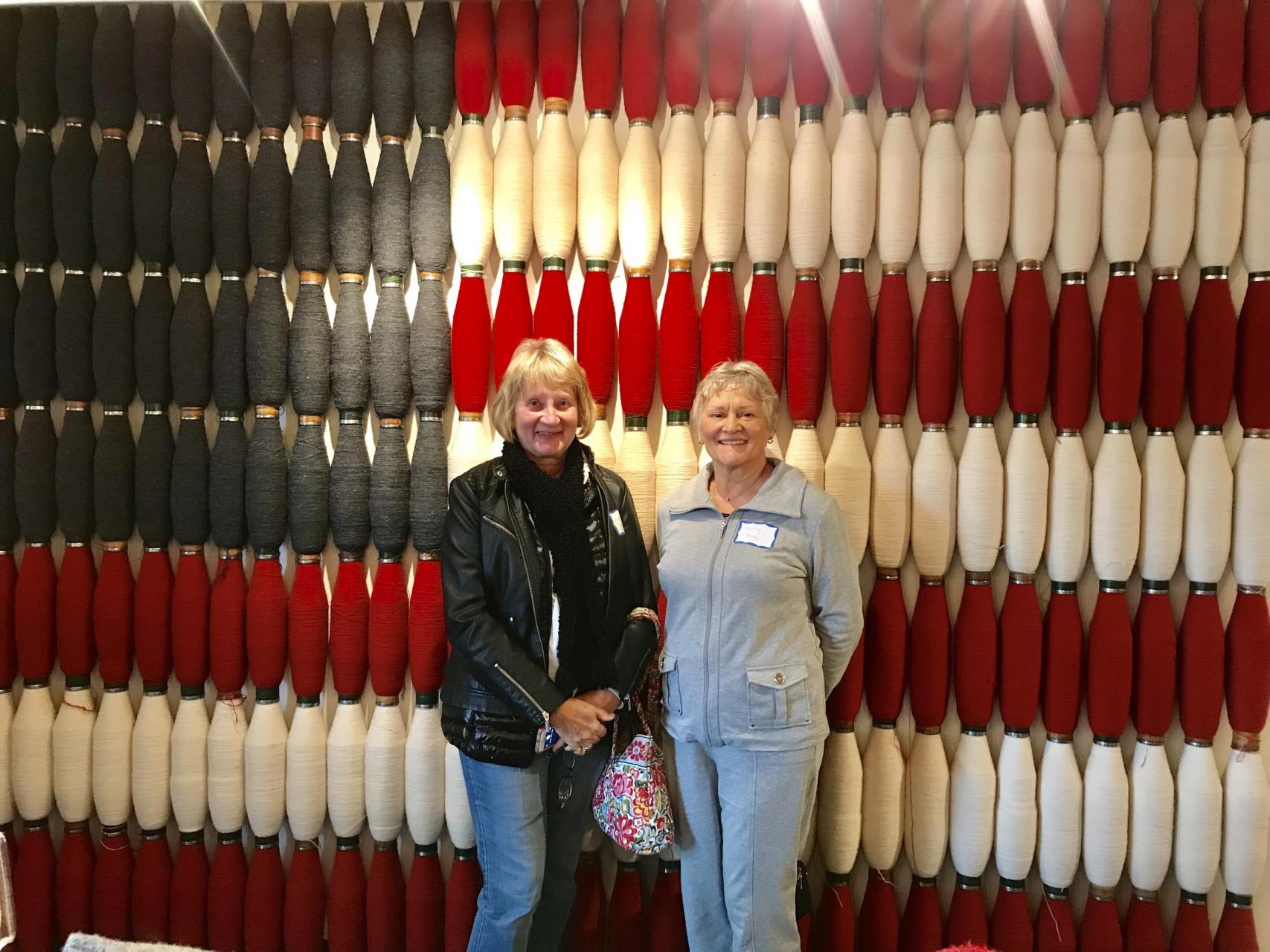 Two women standing in front of spools of yarn.