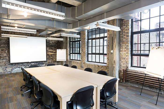 Room with exposed stone walls, a 6-16 person board room table, a projector, and industrial windows.