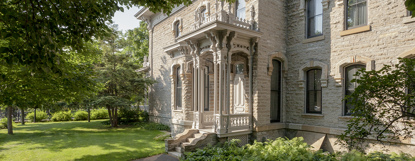 Summertime photo of Alexander Ramsey House, a gray limestone building in the French Second Empire style