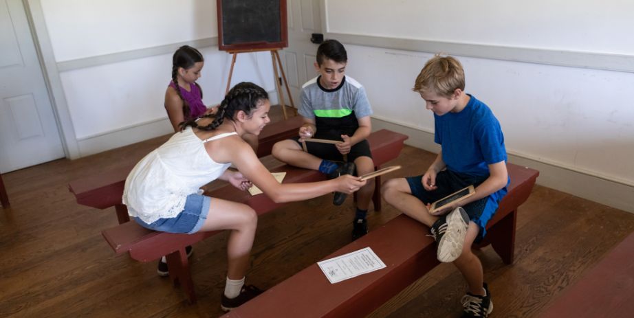 four kids in an old schoolroom play with handheld blackboards