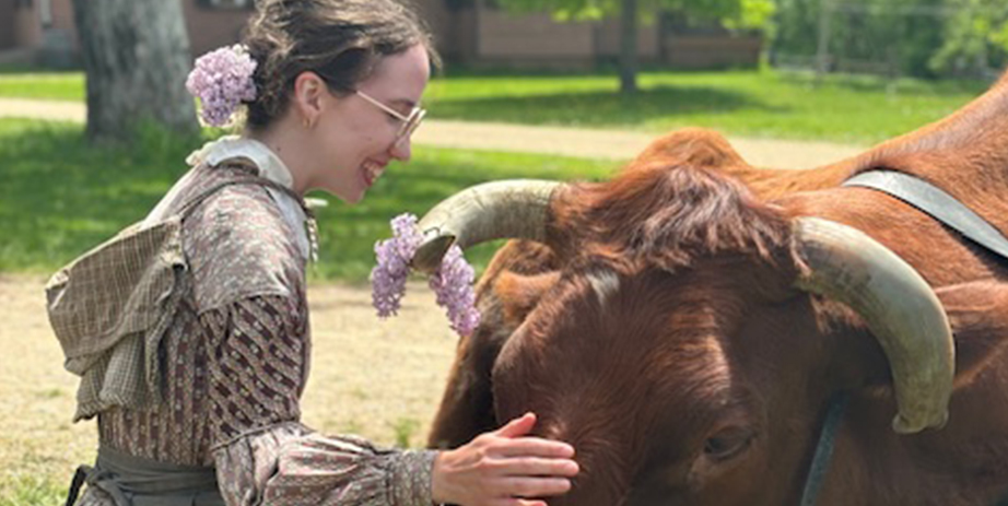 Woman in period clothes petting cow on a sunny spring day