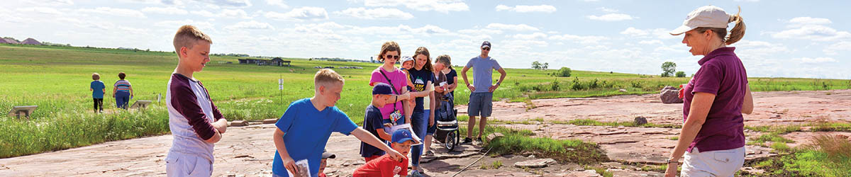 Kids and adults looking at the petroglyphs in a summer day.