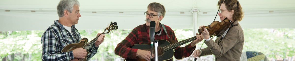 3 musicians playing musical instruments under a big rental tent.