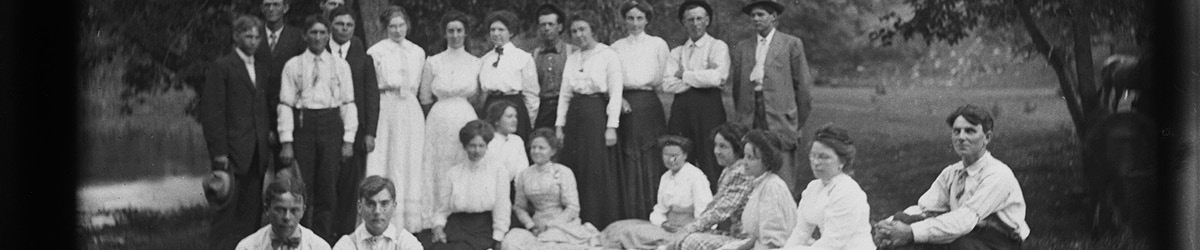 Large group of people sitting and standing next to a river.