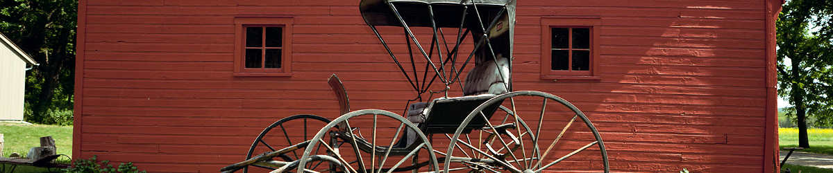 Old carriage resting in front of a red building.