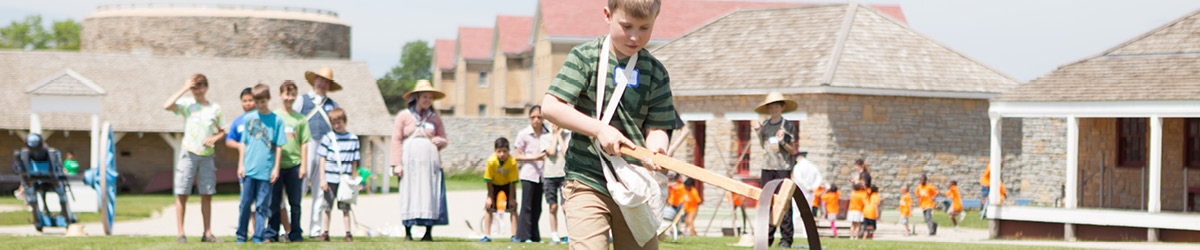A group of children play historic yard games on the lawn of Fort Snelling.