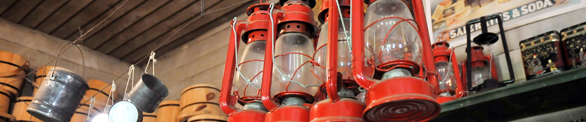 Four red metal oil lamp hanging on the right and several metal buckets on the left.