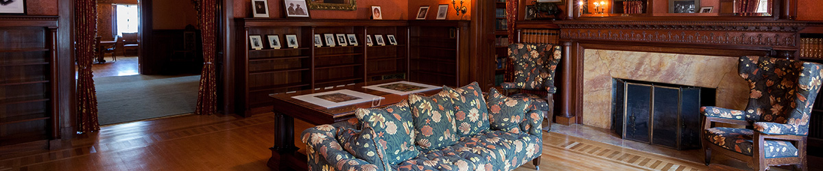 A room with a flowered couch and two matching chairs, fireplace, and shelves with photos