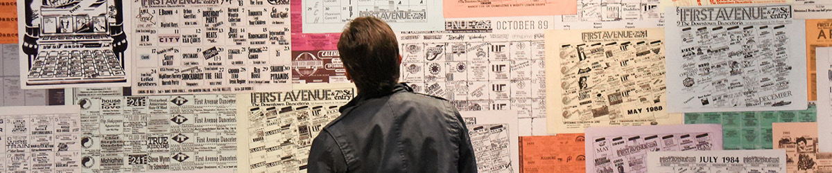 A man looks at music posters on an exhibit wall.