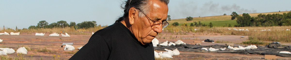 A man wearing glasses looking down the ground, with a red rock prairie in the background.