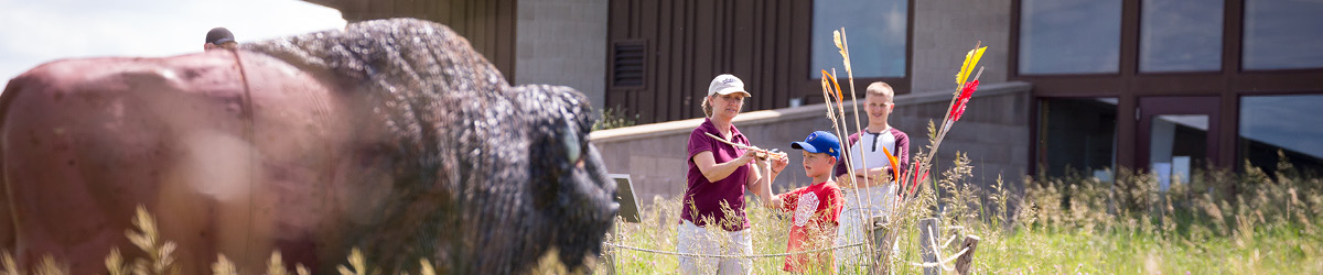 In the background, two boys get assistance from a volunteer in throwing "spears," while a bison replica stands in the foreground.