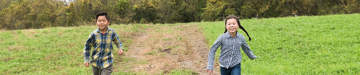 A boy and a girl running on a dirt path toward the camera.