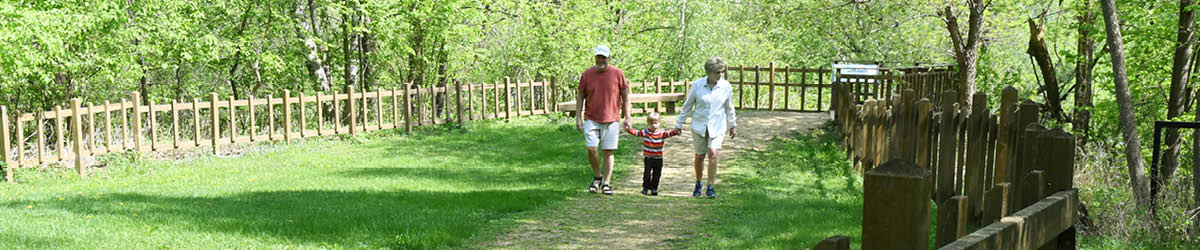 Two adult holding a child's hand on either side, walking in a fenced area.