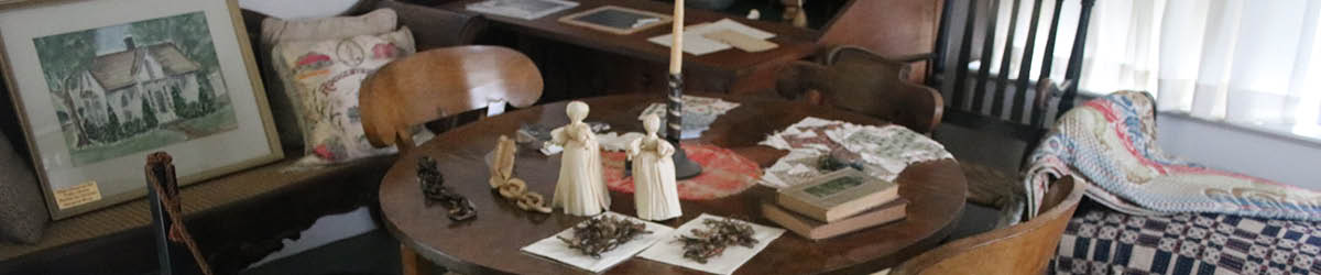 Antique wood table and chairs with a display of quilt squares, handmade dolls, and books.