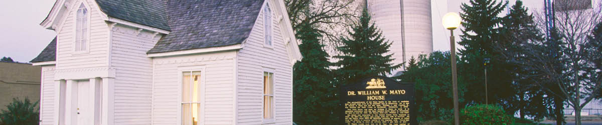 Exterior view of W. W. Mayo House. A small, white house set against green trees with a historical marker in the front yard.